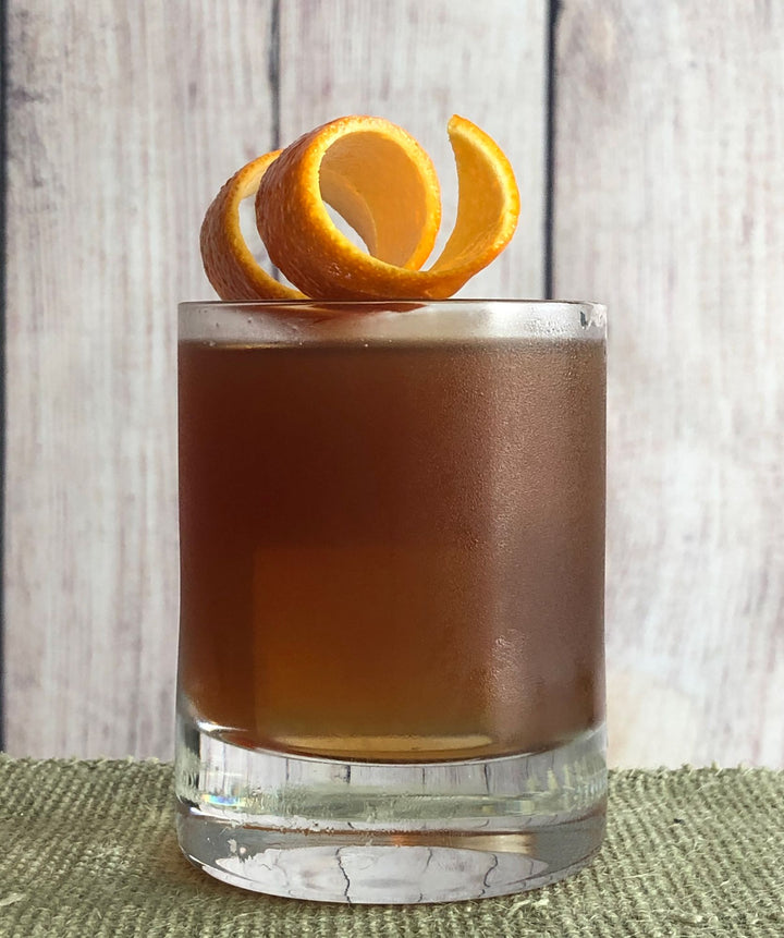 Brown cocktail in a glass with orange garnish on a wooden surface