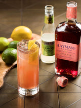 Cocktail with lemon garnish, bottle of Hayman's gin, and tonic on a wooden surface.