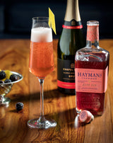 Bottle of Hayman's gin, champagne, and a cocktail on a wooden surface