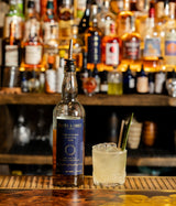 Bottle of Smith & Cross rum on a bar with a cocktail garnished with a straw and lemon peel.