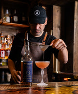 Barista pouring a drink from a bottle labeled 'Smith & Cross' into a glass with a dark wooden bar background.