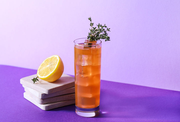 Glass of iced tea with lemon and thyme on a purple surface