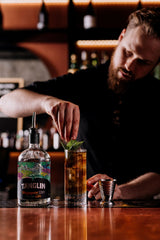 Bartender preparing a cocktail with a bottle of Tanglin gin on a bar counter.