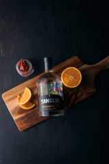 Tanglin gin bottle on a wooden cutting board with orange slices and a cocktail garnish against a dark background