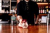 Bartender presenting a cocktail garnished with a flower at a bar.