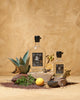 An artful display of The Lost Explorer Tobala Mezcal in two sizes, set against elements of earth and rocks, a cacao bean, an agave plant, and lemons with a textured terracotta background.
