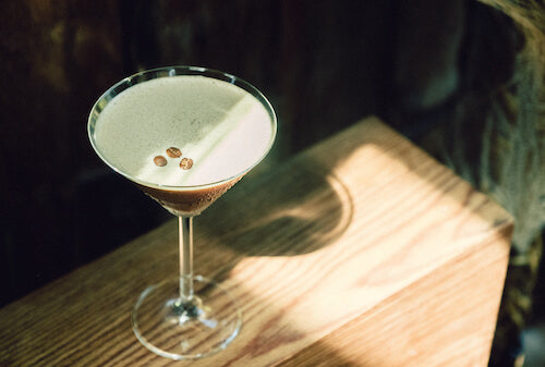 The Nomad's Expresso cocktail, a martini glass with a dark coffee looking liquid, a foamy surface, and three coffee beans as garnish made with Lost Explorer Tobala mezcal.