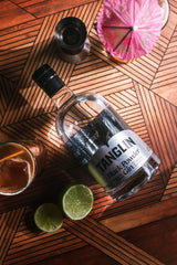 Bottle of Tanglin Black Powder gin on a wooden table with a cocktail shaker and lime wedge.
