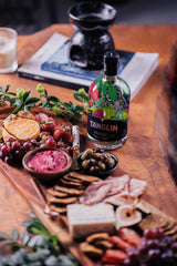 Tanglin gin bottle on a charcuterie board with fruits, cheese, and crackers.