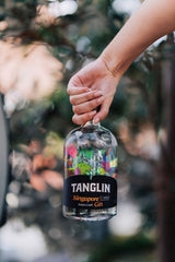 Hand holding a bottle of Tanglin gin with a blurred natural background