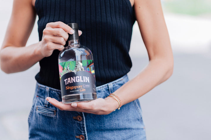Person holding a bottle of Tanglin Singapore Gin against a blurred background