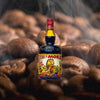 A bottle of Tempus Fugit Creme de Moka against a backdrop of just-roasted coffee beans, wisps of smoke coming off them.
