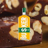Bottle of The Busker Triple Cask Irish Whiskey over backdrop of chocolate nut candy bar.