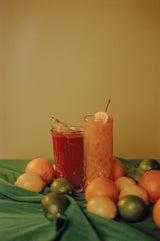 Two glasses of iced tea with fruit on a green cloth against a yellow wall