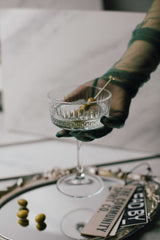 Hand holding a cocktail glass with olives on a reflective surface
