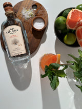 Lost Explorer tequila bottle with a cocktail and citrus fruits on a white surface