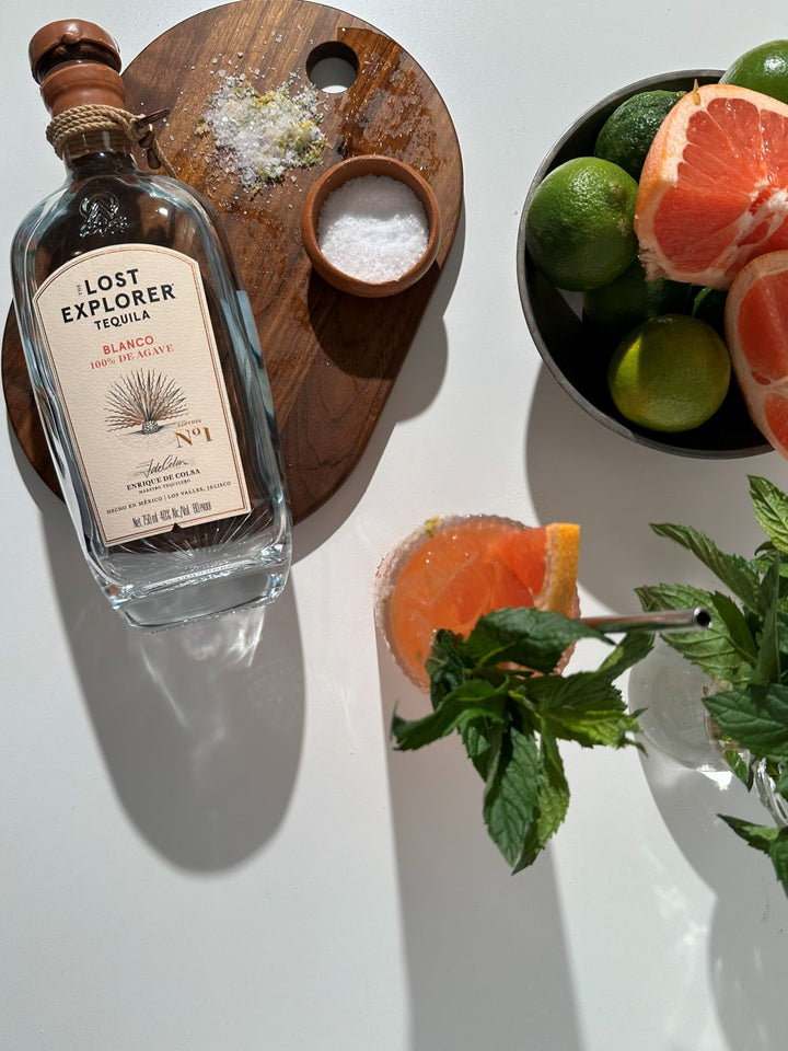 Lost Explorer tequila bottle with a cocktail and citrus fruits on a white surface
