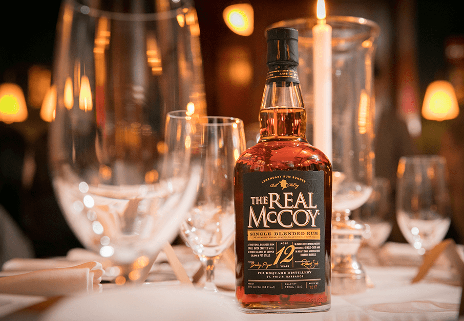 A beautifully set table with candlelight, in the foreground an unopened bottle of The Real McCoy Single Blended Rum Aged 12 Years from Foursquare Distillery.