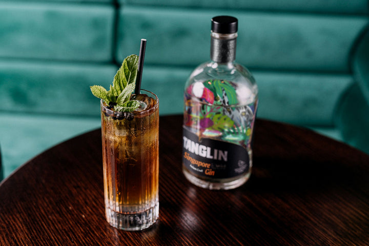 Bottle of Tanglin gin with a cocktail on a wooden table against a teal background