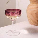 Wine glass with pink liquid on a white surface next to a wooden vase.