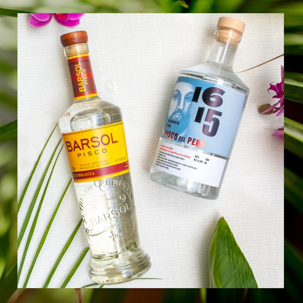 Bottles of Barol Quebranta Pisco and 1615 Pisco laying down on a white cloth next to flowers.