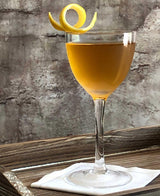 Cocktail in a glass with a lemon twist on a wooden surface.