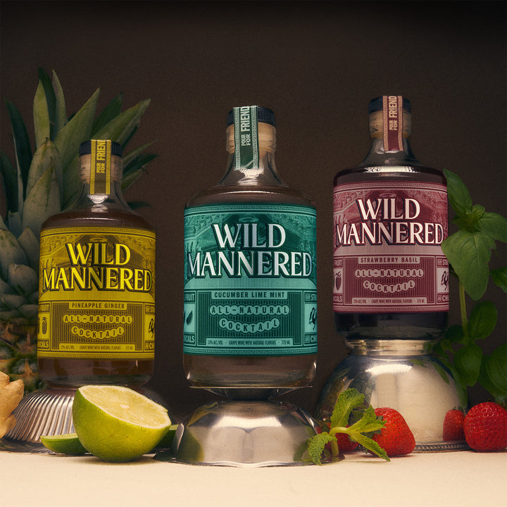 Three bottles of Wild Mannered gin with garnishes on a dark background