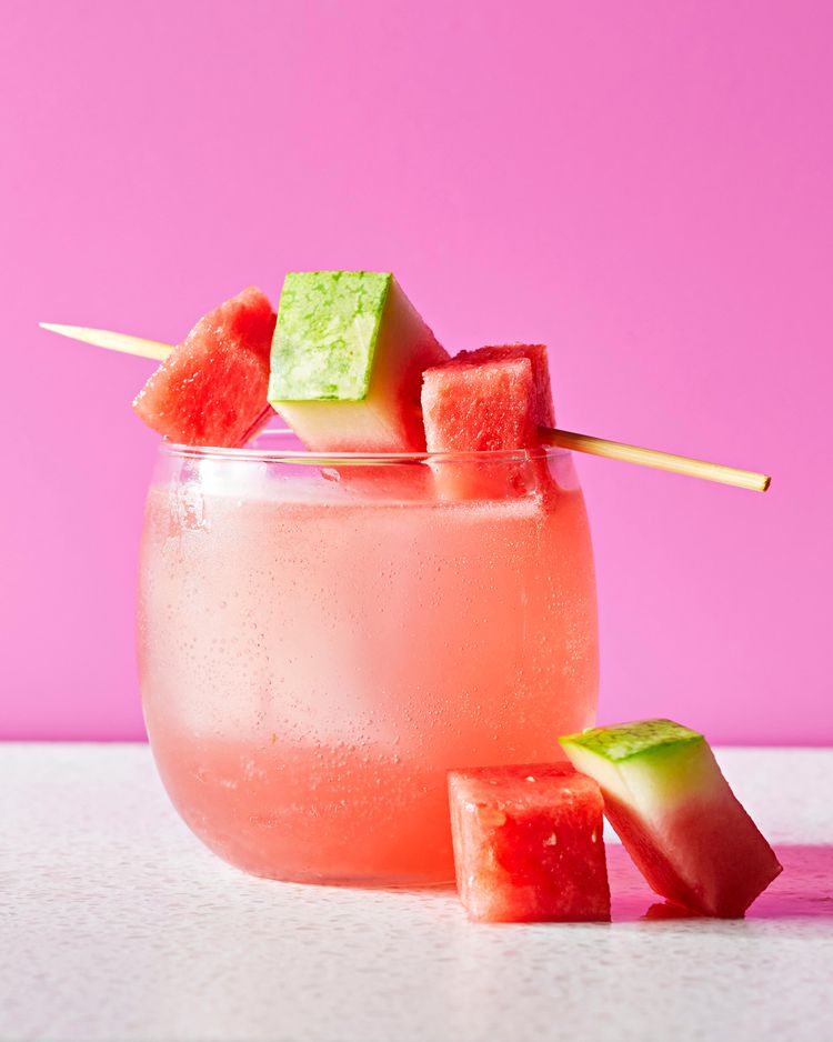 Glass of pink drink with watermelon cubes on a pink background