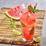 Glass of watermelon mojito with lime wedges on a wooden board
