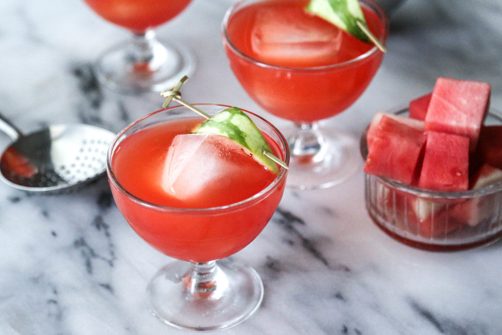 Two glasses of red watermelon gazpacho with ice cubes on a marble surface.
