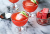 Two glasses of red watermelon gazpacho with ice cubes on a marble surface.
