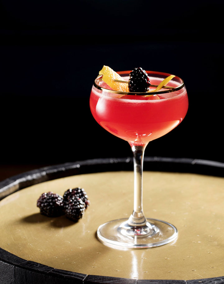 Red cocktail in a glass with blackberries and an orange slice on a dark surface