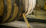 Wooden barrel with liquid being poured into a container, likely in a brewery or distillery setting.