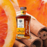 A stout, shapely bottle of appealing amber liquid with a wooden cap. The label is to the left and reads Small Batch Kentucky Straight Bourbon Whiskey Bottled in Bond with Wilderness Trail written down the right in script. All against a backdrop of macro image of appealing oranges slices and a bundle of fragrant cinnamon.