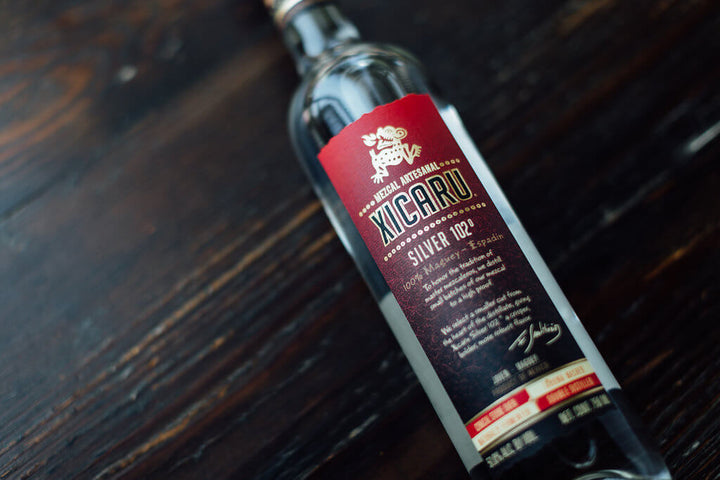 A hero image of Xicaru Silver 102, a close-up of the label reading Mezcal Artesanal. "To honor the tradition of master mezcaleros, we distille small batches of our mezcal to a high proof. We select a smaller cut from the heart of the distillate, giving Xicaru Silver 102 a crisper, richer, more robust flavor."