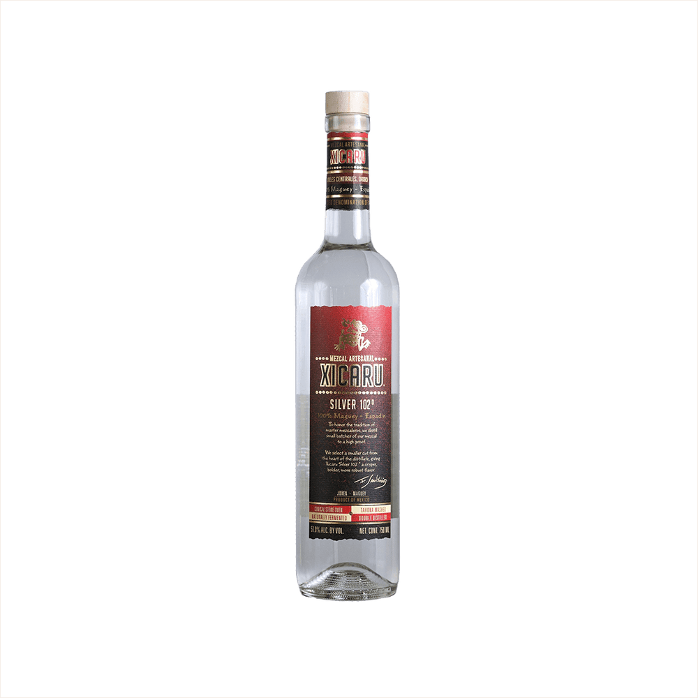 A tall artesanal shaped bottle with a red label and gold writing stating: Xicaru Mexcal Silver 102 Proof