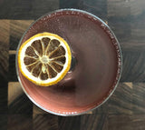 Cocktail with a dried lemon wheel garnish on a reflective surface