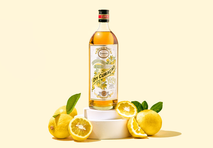 Bottle of Ferrand Yuzu Curacao with lemons on a light yellow background