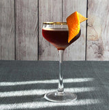 Cocktail in a glass with an orange twist on a textured surface with wooden background