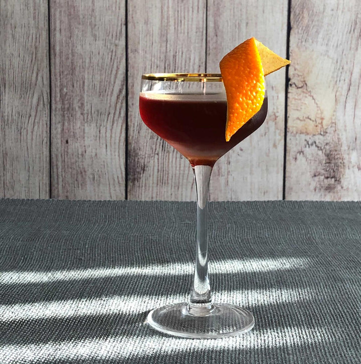 Cocktail in a glass with an orange twist on a textured surface with wooden background