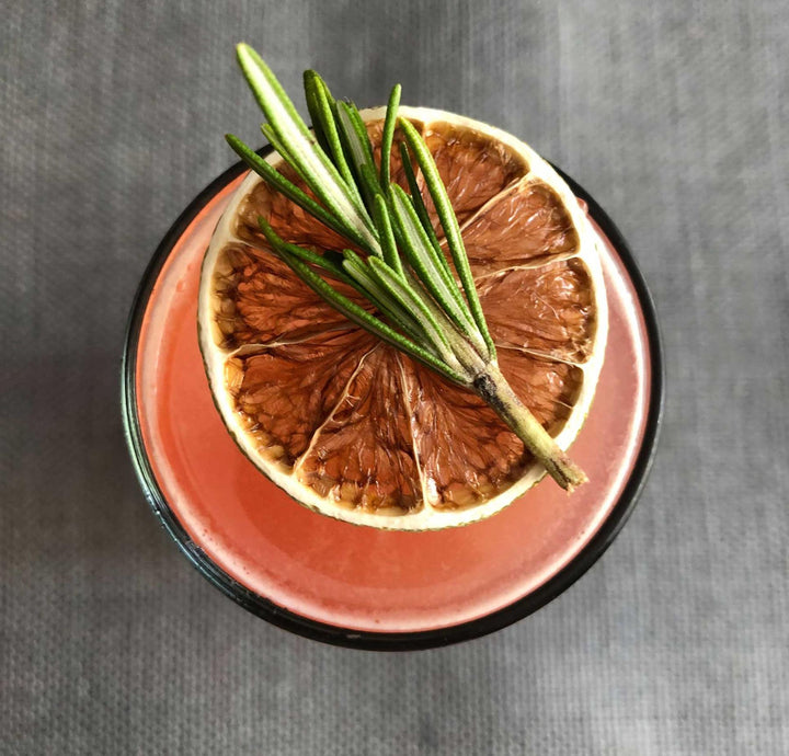 Dried citrus fruit with rosemary on a pink plate against a gray background