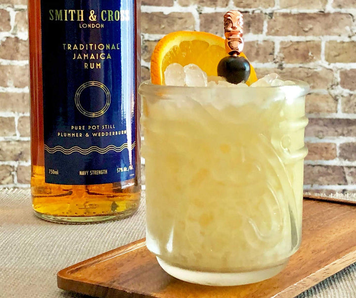 Cocktail with ice and garnish next to a bottle of Smith & Cross Traditional Jamaica Rum on a wooden tray.