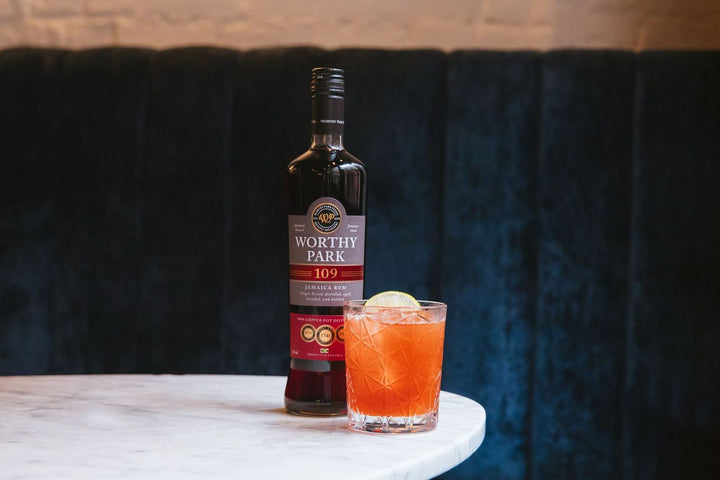Bottle of Worthy Park 109 rum with a cocktail on a marble surface against a dark background