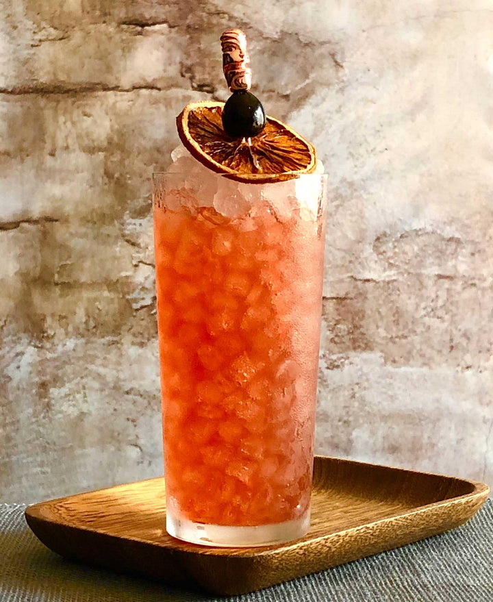 Cocktail with a garnish on a wooden tray against a textured wall background