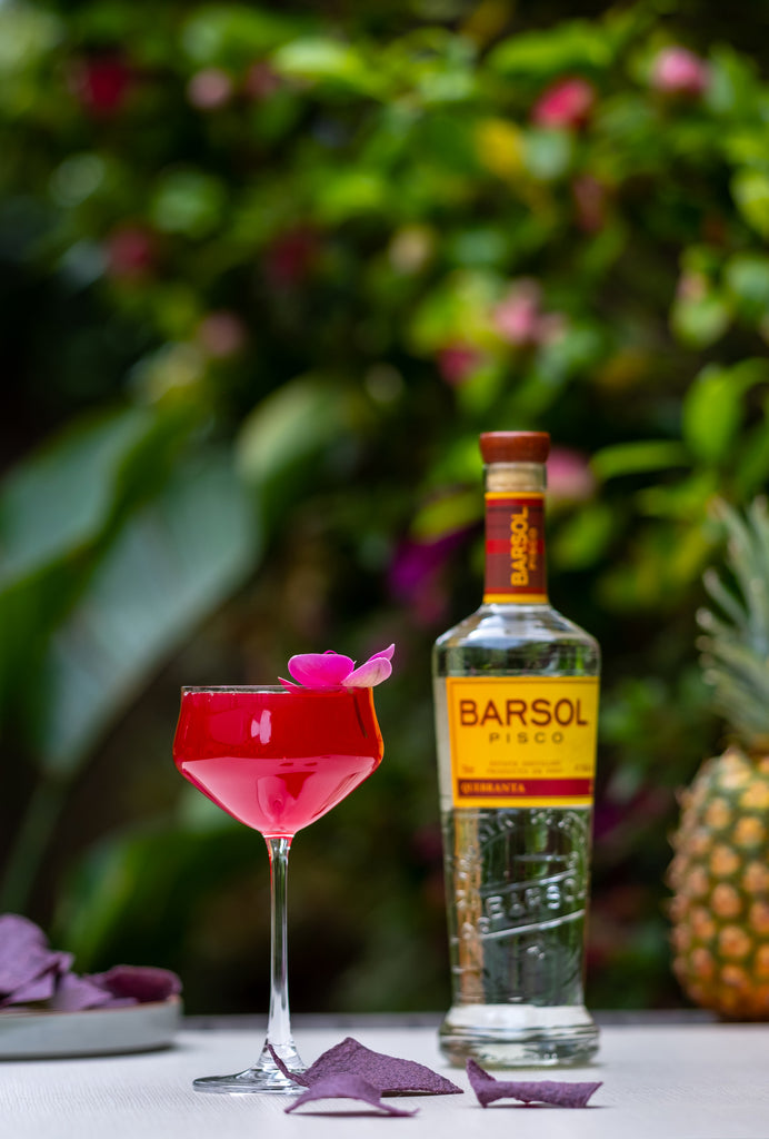 Bottle of Barsol Quebranta Pisco on a table outside next to a red cocktail.