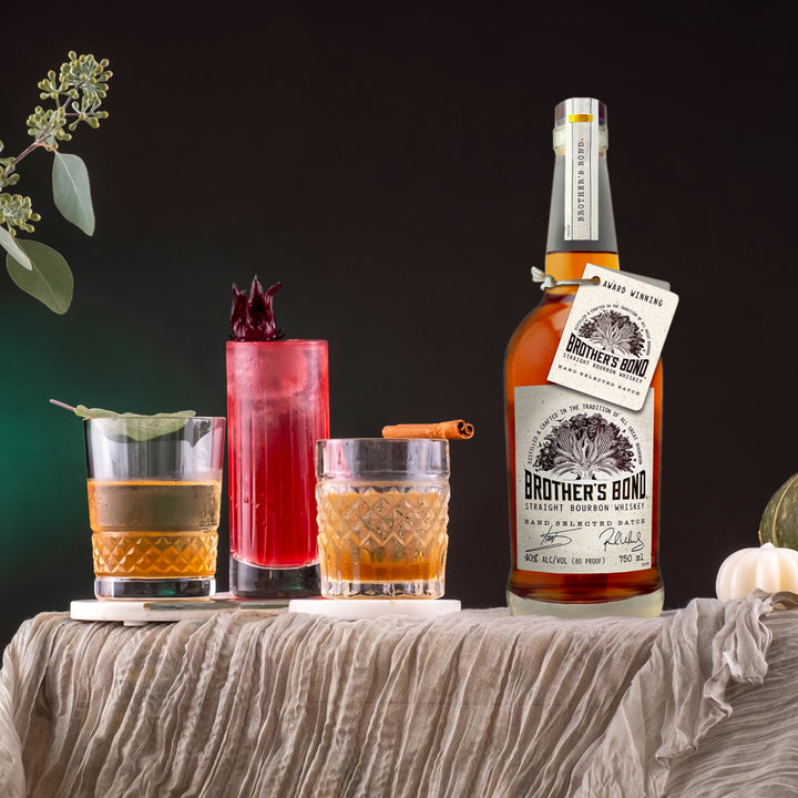 Bottle of Brother’s Bond Straight Bourbon Whiskey on a table next to 3 cocktails.