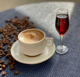 Cappuccino in a white cup with a glass of red wine and coffee beans on a textured surface