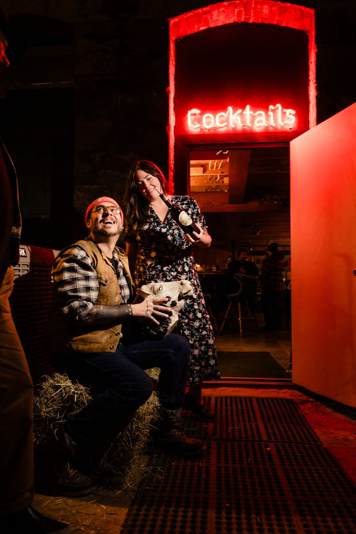 Two people in a dimly lit bar with a 'Cocktails' neon sign.