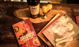 Cocktail book titled 'Necron Cocktail' on a wooden table with a bottle and glasses.