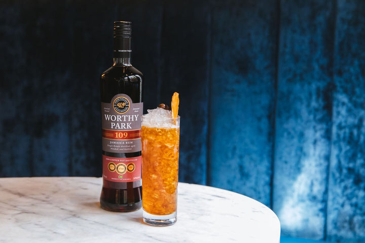 Bottle of Worthy Park 109 rum with a cocktail on a marble surface against a blue textured background